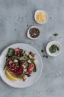Vista dall'alto di piatti e ciotola con deliziosa insalata di lenticchie con cetrioli e spinaci posizionati vicino a tovaglioli sul tavolo grigio — Foto stock