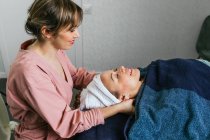 Side view of content masseuse massaging shoulders of female client lying on table in beauty salon — Stock Photo