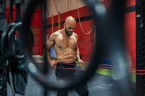 Muscular bearded man pulling elastic rope with effort during functional workout in modern gym — Stock Photo