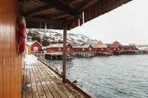 Caminho de madeira com gaivotas que vão perto da parede de cabana na aldeia costeira perto do cume montês nevado no dia de inverno em Ilhas Lofoten, Noruega — Fotografia de Stock