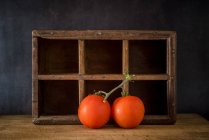 Branch of fresh tomatoes placed on wooden table on dark background in studio — Stock Photo