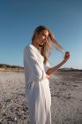 Femme blonde aux cheveux longs debout sur la plage regardant loin — Photo de stock