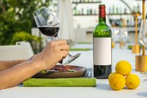 Bouteille de vin et client tenant un verre au restaurant de haute cuisine en plein air — Photo de stock