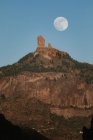 Paisagem espetacular com grande lua cheia no céu azul sobre o pico da montanha rochosa com floresta verde na noite de verão — Fotografia de Stock