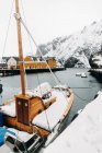 Wooden sailboat covered with snow floating on water against cottages and mountains on winter day in fjord town on Lofoten Islands, Norway — Stock Photo