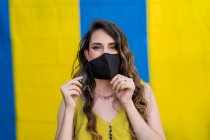 Zufriedene Frau mit welligem Haar trägt Schutzmaske während Coronavirus in der Stadt Blick auf Kamera auf zwei farbigen Hintergrund — Stockfoto