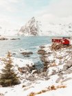 Cabañas rojas situadas en la costa nevada de la cordillera en las Islas Lofoten, Noruega - foto de stock