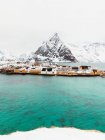 Cold sea with tranquil water located near coastal settlement and snowy mountain ridge on overcast winter day on Lofoten Islands, Norway — Stock Photo