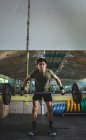 Сосредоточенный азиатский спортсмен делает тягу с тяжелым штангой во время тренировки в тренажерном зале, смотря в камеру — стоковое фото