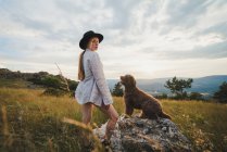Side view of female owner with obedient Labradoodle dog sitting on rock in mountains looking at camera — Stock Photo
