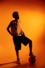 Mulher preta com roupa de basquete no estúdio usando géis de cor e luzes do projetor sobre fundo laranja — Fotografia de Stock