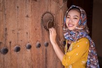 Asian woman with headscarf next to an old wooden door — Stock Photo