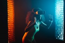 Анонимные удивленные этнические женщины с открытым ртом исследуют виртуальную реальность в наушниках на черном фоне — стоковое фото