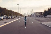 Vista trasera de la mujer viajera caminando por una avenida con Dubai Marina en el fondo - foto de stock
