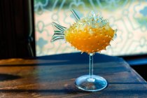 Bebida alcoólica amarela brilhante fantasia criativa servida em copo de cocktail de peixe fugu no balcão de madeira bar — Fotografia de Stock