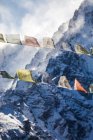 Ряди барвистих буддійських молитовних прапорів висять на канатах на тлі скелястих Гімалаїв, покритих снігом взимку в Непалі. — стокове фото