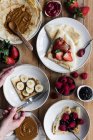 Top view of anonymous person taking bowl of tasty crepes with assorted toppings placed on lumber table during breakfast — Stock Photo