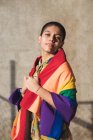 Junge bisexuelle ethnische Frau mit bunter Flagge, die in die Kamera blickt und LGBTQ-Symbole an sonnigen Tagen darstellt — Stockfoto