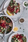 Вид зверху на тарілки і миску зі смачним сочевичним салатом з огірками і шпинатом, розміщеним біля серветок на сірому столі — стокове фото