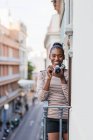 Inhalt ethnische Frau in Tracht mit gestreiftem Ornament mit professionellem Fotogerät, das tagsüber auf dem Balkon in die Kamera schaut — Stockfoto
