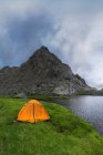 Orangefarbenes Zelt am grasbewachsenen Ufer der Laguna Grande gegen die Sierra de Gredos und bewölkten Himmel in Avila, Spanien — Stockfoto