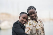 Содержание стильные афро-американские дамы оставаться рядом и смотреть на камеру с вдумчивой улыбкой в парке в яркий день — стоковое фото