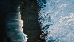 Вид беспилотника на захватывающий пейзаж пенных морских волн, разбивающихся на грубом скалистом побережье — стоковое фото