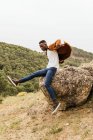 Modelo masculino afro-americano na moda na roupa da moda pulando de pedra em terras altas — Fotografia de Stock