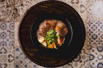 Зверху темна миска з красивою порцією яловичих овочів, розміщених на дерев'яному лотку — стокове фото
