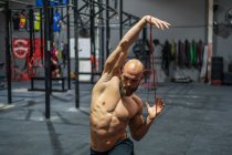 Homme barbu torse nu regardant loin étirement élastique bande avec les bras et de fente pendant l'entraînement fonctionnel dans la salle de gym — Photo de stock