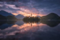 Spettacolare scenario di laghetto calmo con isola e castello situato in altopiani rocciosi in Slovenia durante il tramonto — Foto stock