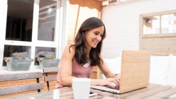 Content female freelancer sitting at table on terrace and typing on laptop while working on remote project — Stock Photo