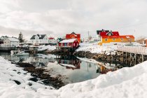 Verschneiter Kai in ruhiger Küstensiedlung mit roten Häusern an bewölkten Wintertagen auf den Lofoten, Norwegen — Stockfoto