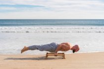 Side view of bald strong athlete doing parallel handstand with bars working out on sandy coast — Stock Photo