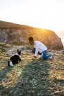 Side view of young African American female owner with toy in hand playing with Border Collie dog while spending time together on beach near waving sea at sunset — Stock Photo