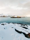 Сніжна скеля, що виходить на острів посеред бурхливого моря з хмарним небом у зимовий день на Лофотенських островах (Норвегія). — стокове фото