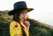 Attractive young female in yellow sundress and hat standing on verdant grassy meadow in sunny countryside — Stock Photo