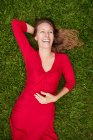 Mujer vestida de rojo tendida en el suelo en un parque con hierba - foto de stock