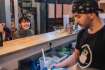 Asian woman in casual wear sitting at counter and talking with male worker of modern ramen bar — Stock Photo