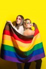 Seitenansicht von multirassischen Freundinnen mit kreativem Make-up, die LGBT-Flagge vor gelbem Hintergrund demonstrieren — Stockfoto