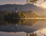 Spectacular scenery of calm pond with island and castle located in rocky highlands in Slovenia during sunset — Stock Photo