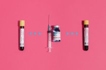 Dall'alto coronavirus esame del sangue negativo e positivo vicino alla fiaschetta di vaccino e siringa su sfondo rosa — Foto stock