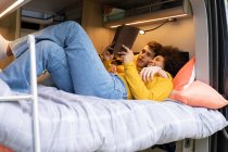 Diverso jovem homem e mulher abraçando e lendo livro interessante enquanto relaxa na cama em van durante a viagem de carro — Fotografia de Stock