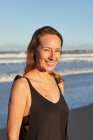 Sorridente femmina in abito estivo in piedi sulla spiaggia sabbiosa e guardando la fotocamera — Foto stock