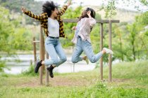 Пара лесбійських багатоетнічних жінок стрибають над землею в лісі і насолоджуються свободою разом — стокове фото
