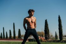 Hemdloser männlicher Athlet mit Tätowierung und breiten Beinen beim Training auf der Wiese — Stockfoto