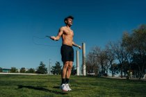 Чоловік-спортсмен в оголеному торсі стрибає з пропускаючою мотузкою і дивиться на прогулянку під час кардіо-тренувань у парку — стокове фото