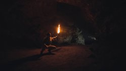 Aventureiro masculino irreconhecível com tocha ardente brilhante agachado enquanto explora caverna subterrânea escura durante a expedição de espeleologia — Fotografia de Stock