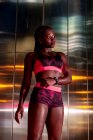 Гидке афроамериканське спортсменка, що стоїть біля металевої стіни і дивиться уночі. — стокове фото