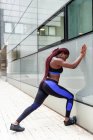 Seitenansicht einer jungen muskulösen ethnischen Frau, die sich beim Training auf der Straße an die Wand lehnt — Stockfoto